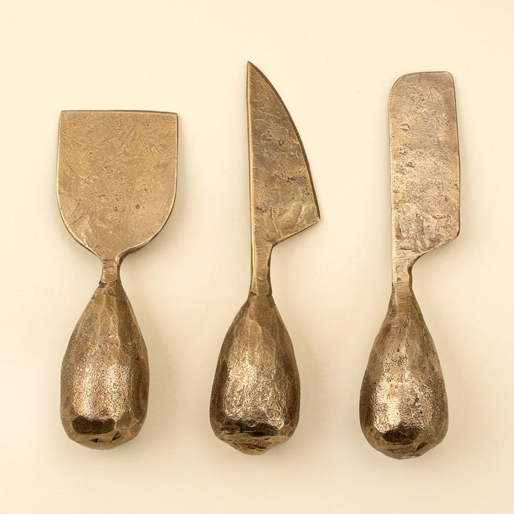Indaba Rotunda hand-forged cheese knife set with three iron cheese knives on a wooden cheese board.