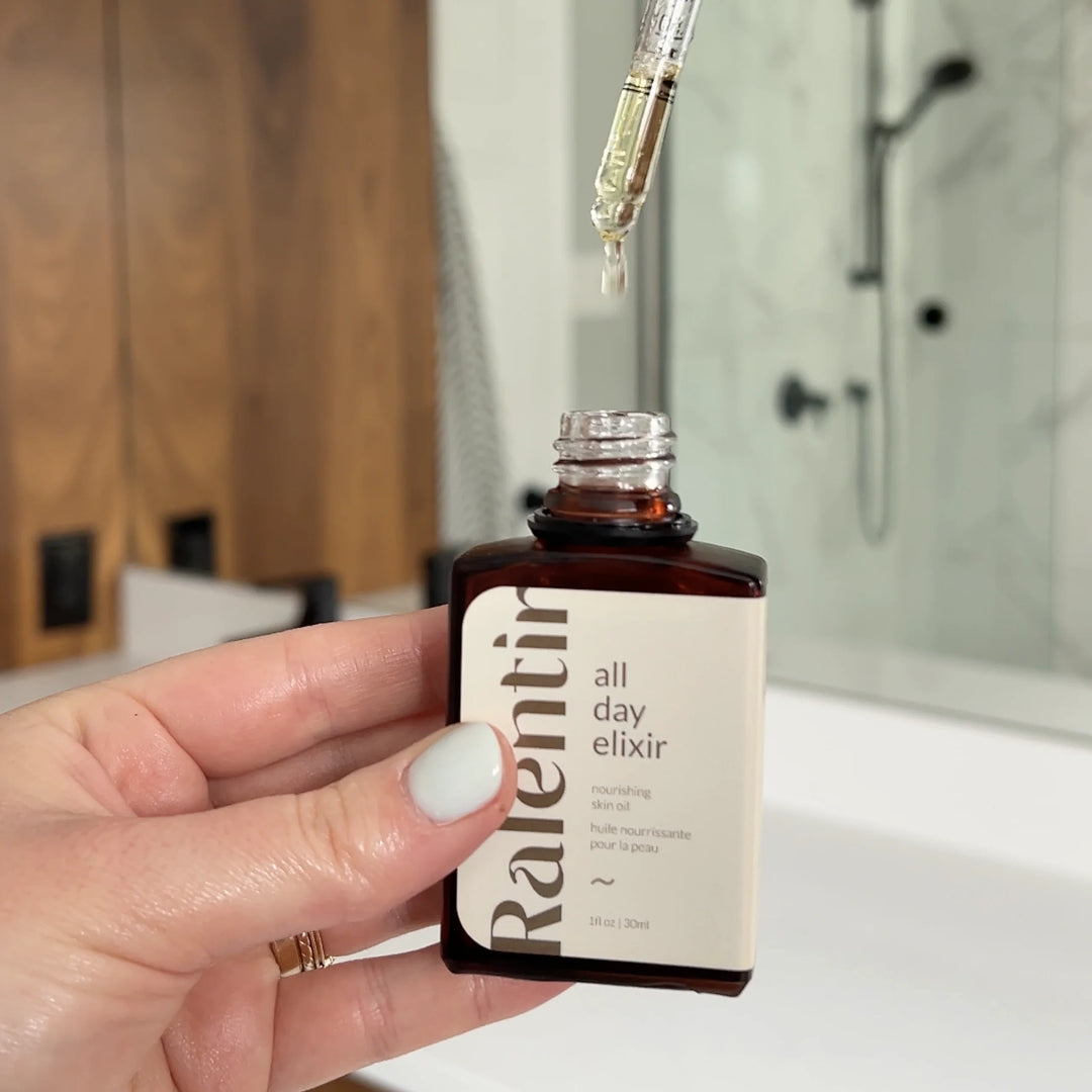 Bottle of All Day Natural Skincare Elixir with dropper, showcasing clear liquid in a sleek glass container.
