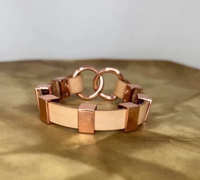 Rose gold  and leathetr bracelet on a reflective surface with a neutral background