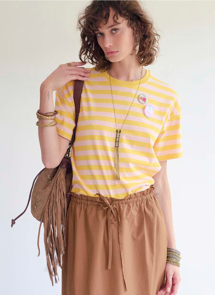 Woman wearing a yellow and white striped shirt with a brown leather suede fringe bag and pants against a light background