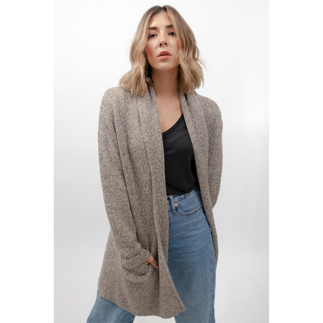 Woman wearing a beige cardigan over a black top and blue jeans on a white background