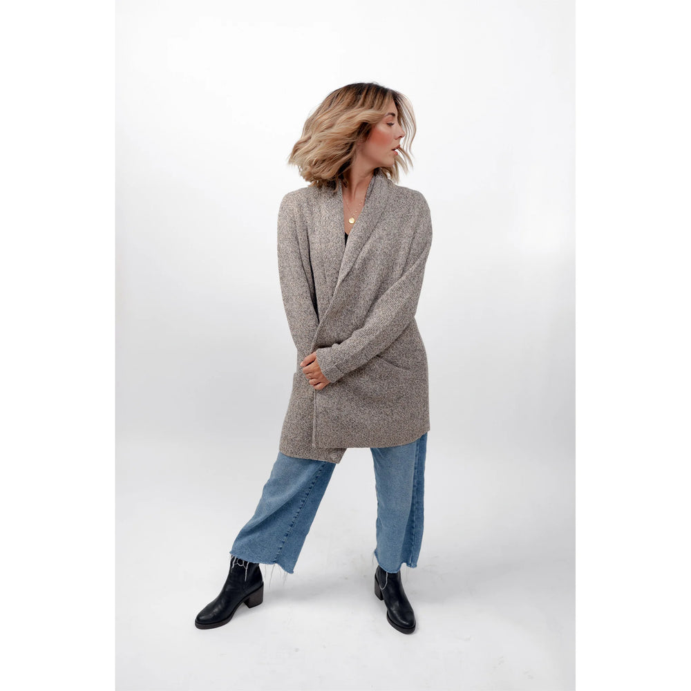 Woman wearing a gray cardigan, blue jeans, and black boots on a white background