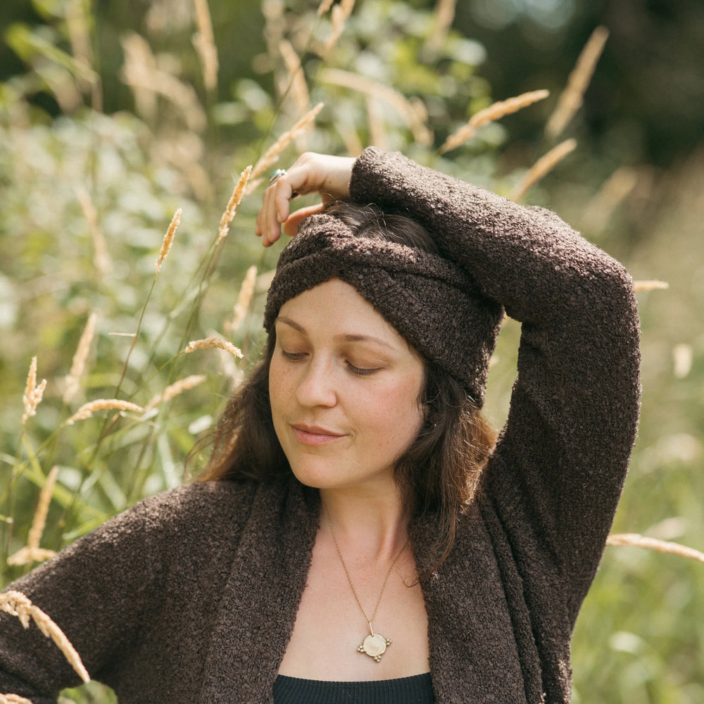 Woman wearing a brown knitted headband and cardigan in a natural setting