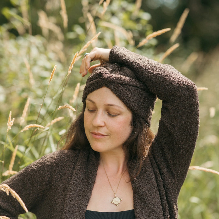 Woman wearing a brown knitted headband and cardigan in a natural setting