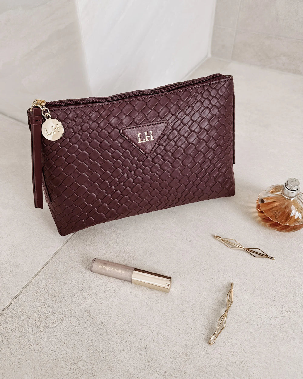 Maroon textured pouch with 'LH' logo on a light surface with lip gloss and perfume bottle.