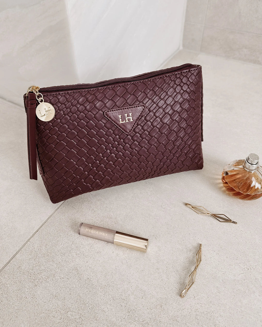 Maroon textured pouch with 'LH' logo on a light surface with lip gloss and perfume bottle.