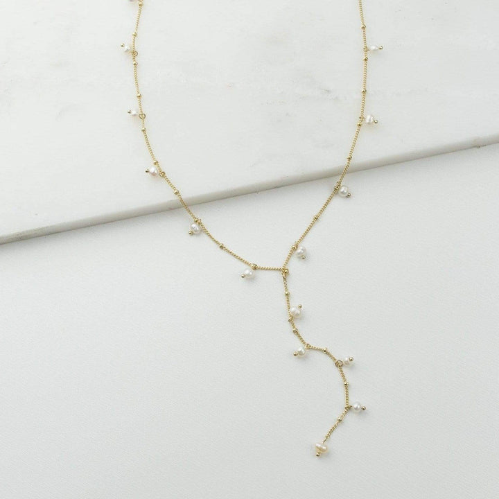 Lover's Tempo Dot Pearl Gold Lariat Necklace featuring a delicate chain with pearl accents and elegant gold detailing.