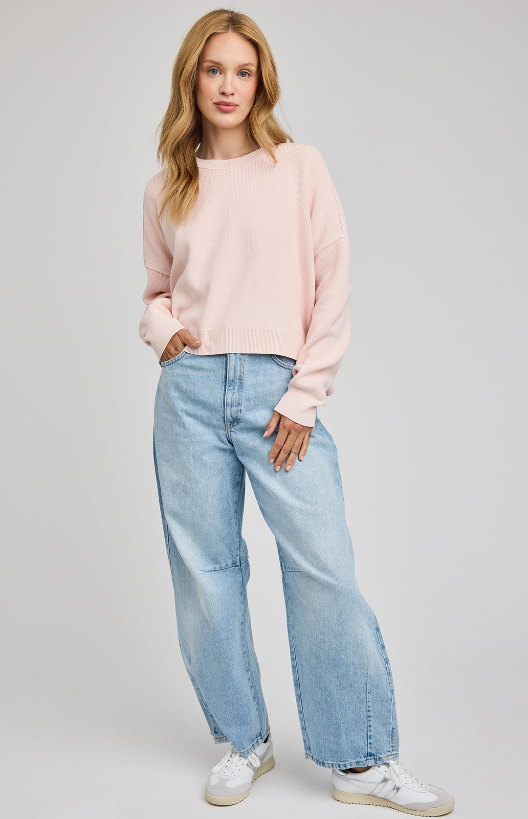 Woman wearing a light pink sweater and blue jeans on a gray background
