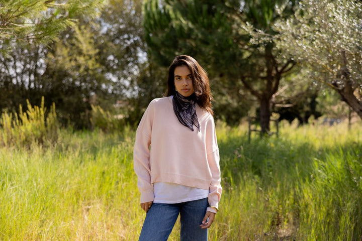 Woman wearing a soft pink sweater standing in a field with trees in the background