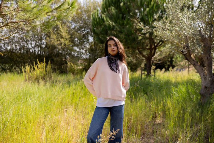 Woman wearing soft pink sweater standing in a field with trees in the background
