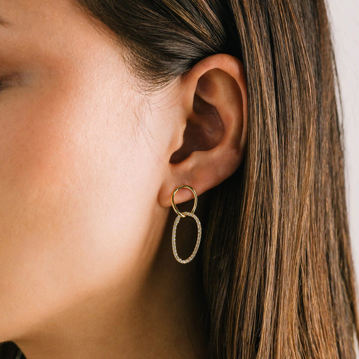 Close-up of an ear wearing a gold hoop earring with a neutral background