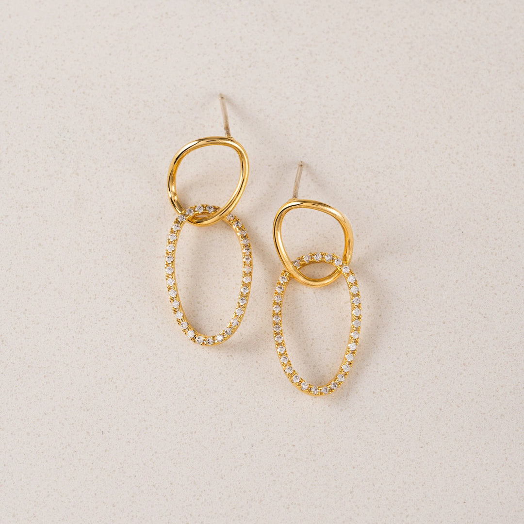 Gold hoop earrings with embedded stones on a beige background