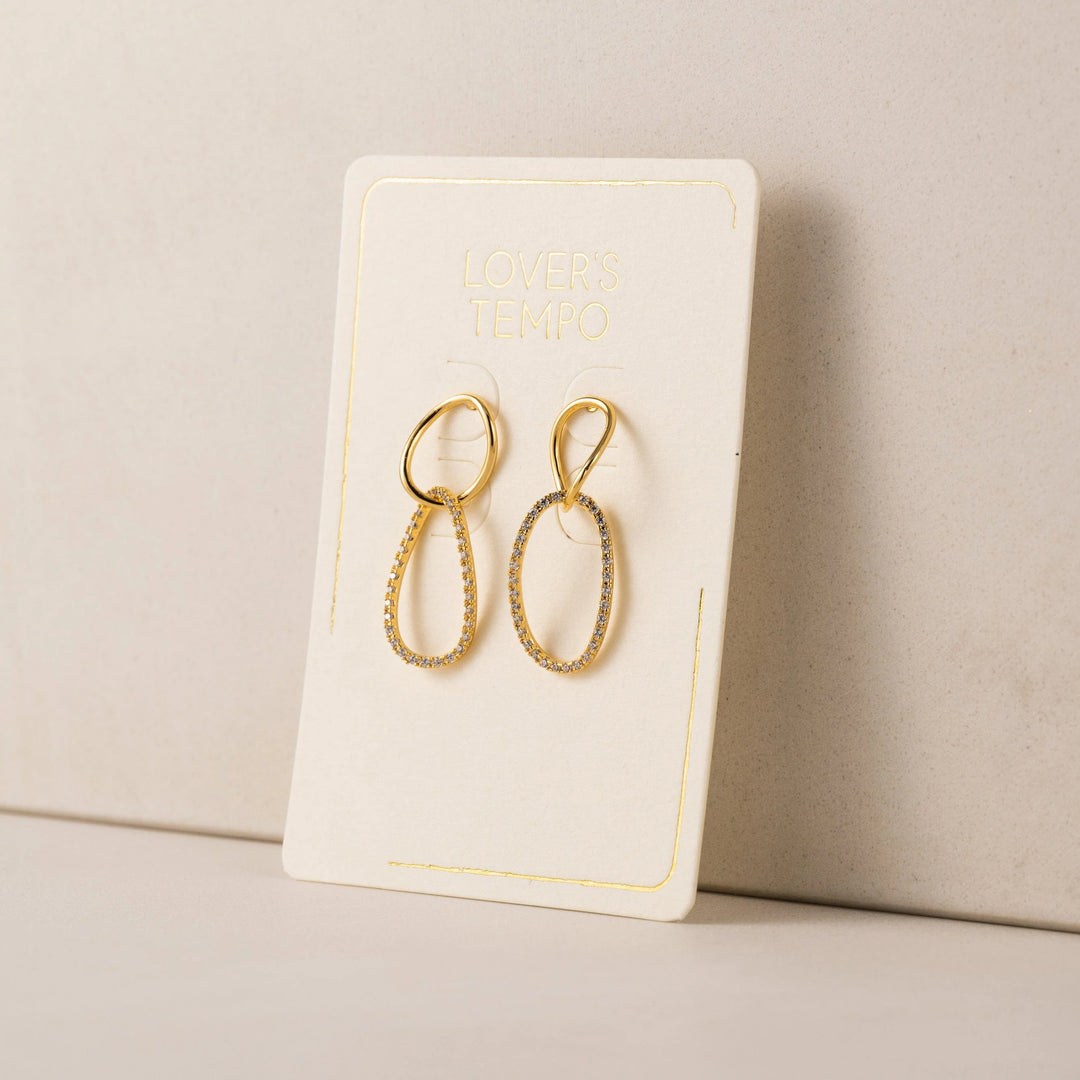 Gold earrings on a branded earring card against a beige background