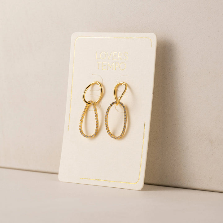 Gold earrings on a branded earring card against a beige background