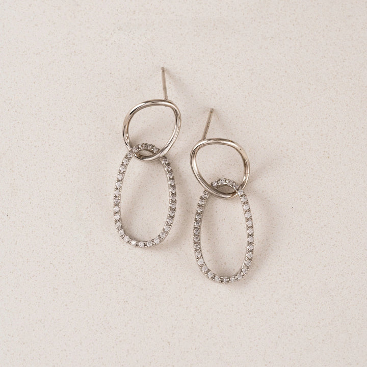Pair of silver hoop earrings with embedded stones on a beige background