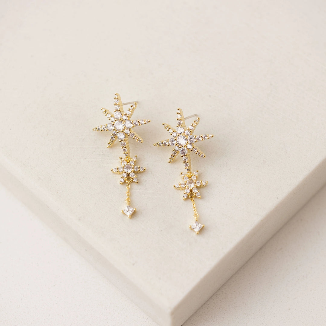 Gold star-shaped earrings on a beige background