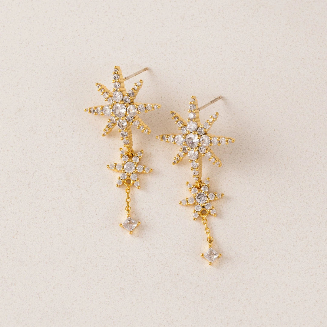 Gold star-shaped earrings with clear stones on a beige background