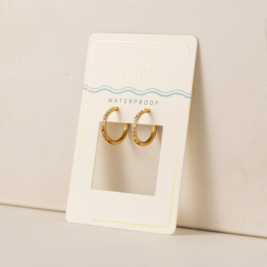Gold hoop earrings on a branded card with 'Waterproof' text on a beige background