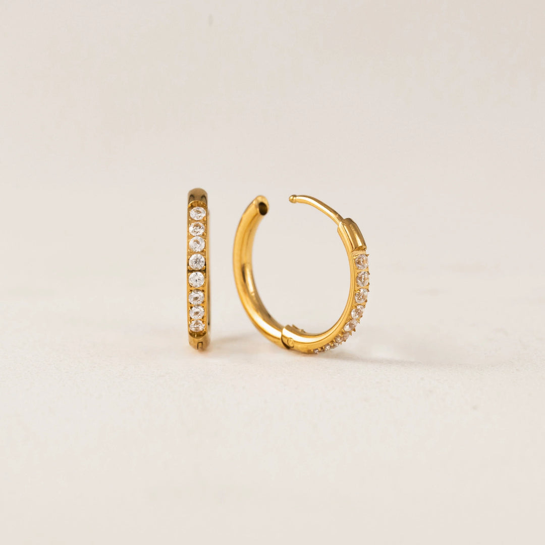 Gold hoop earrings with embedded diamonds on a light beige background