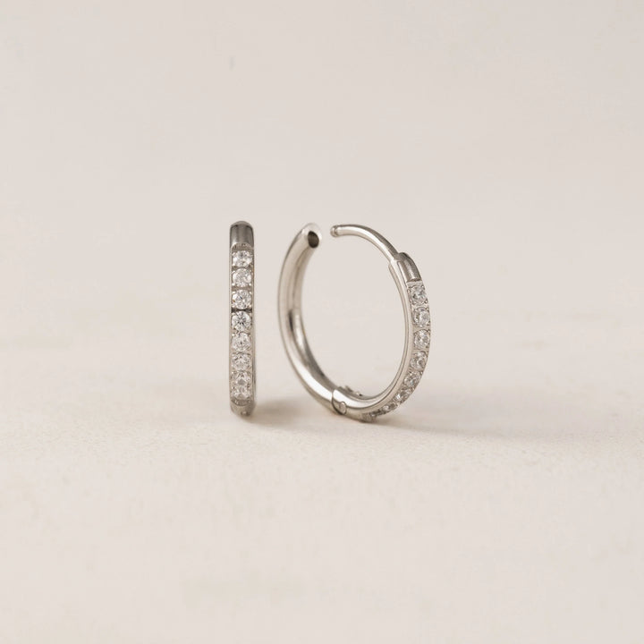 Silver hoop earrings with embedded stones on a beige background