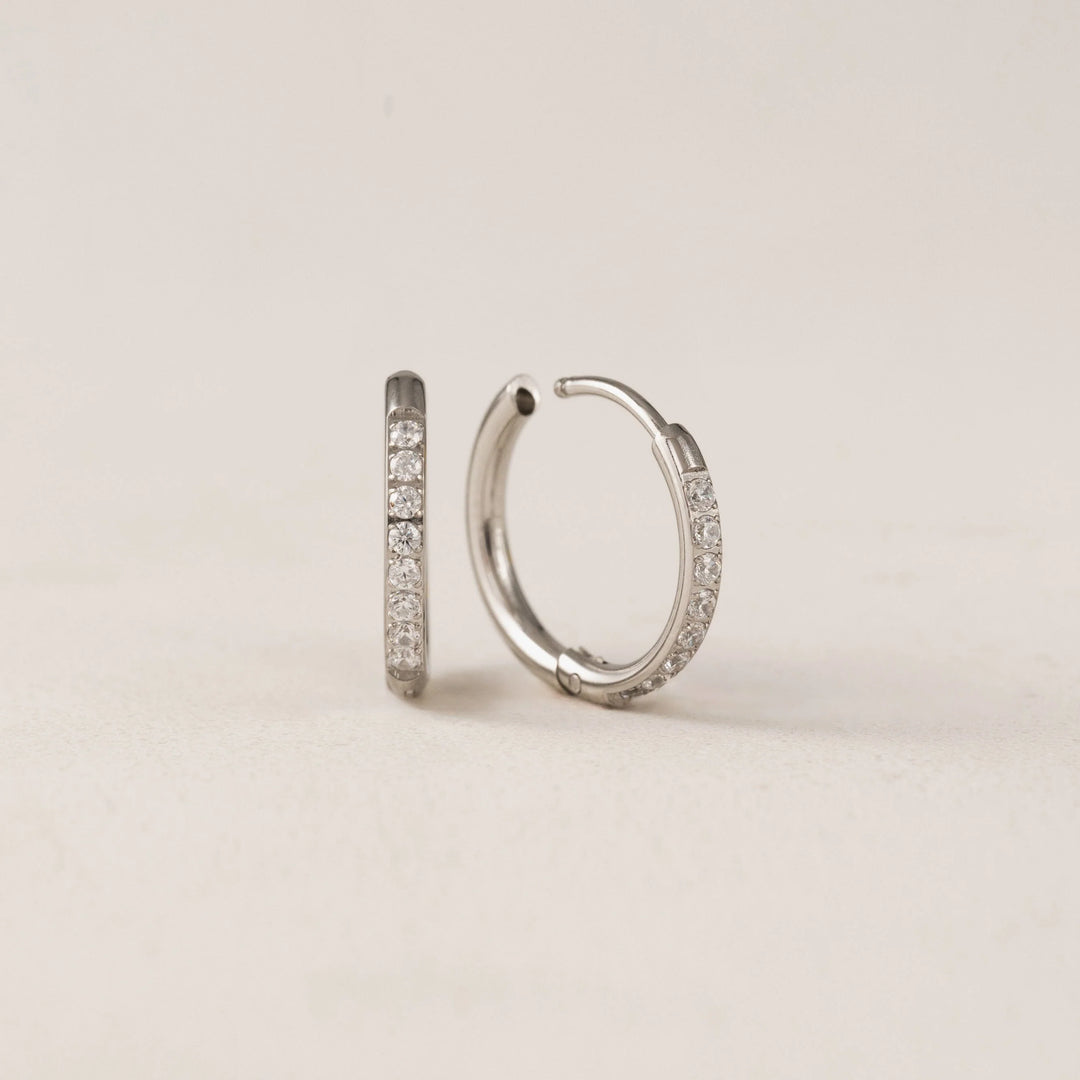 Silver hoop earrings with embedded stones on a beige background