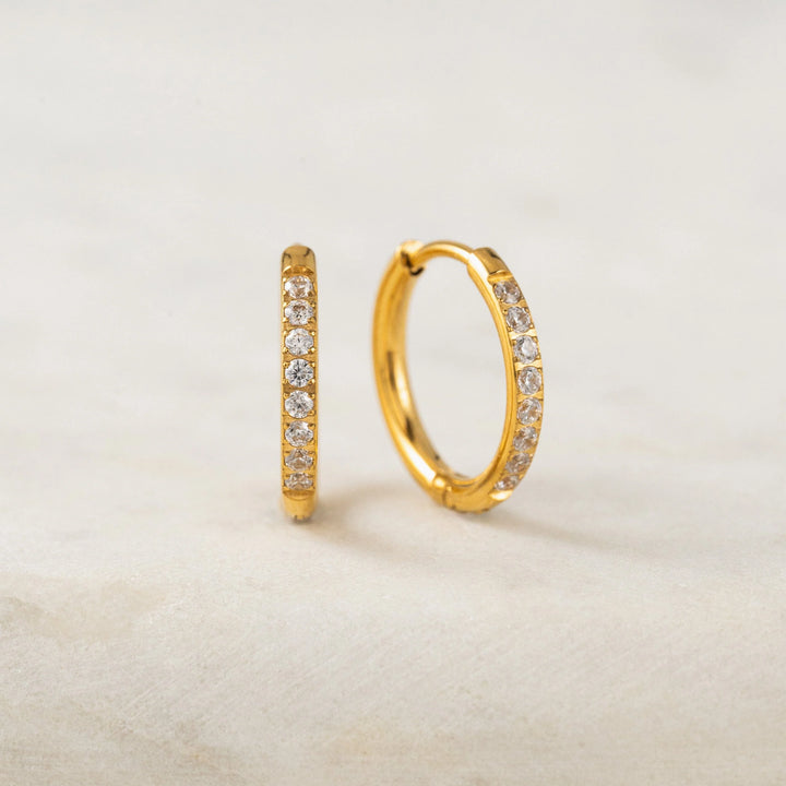 Gold hoop earrings with embedded diamonds on a beige background