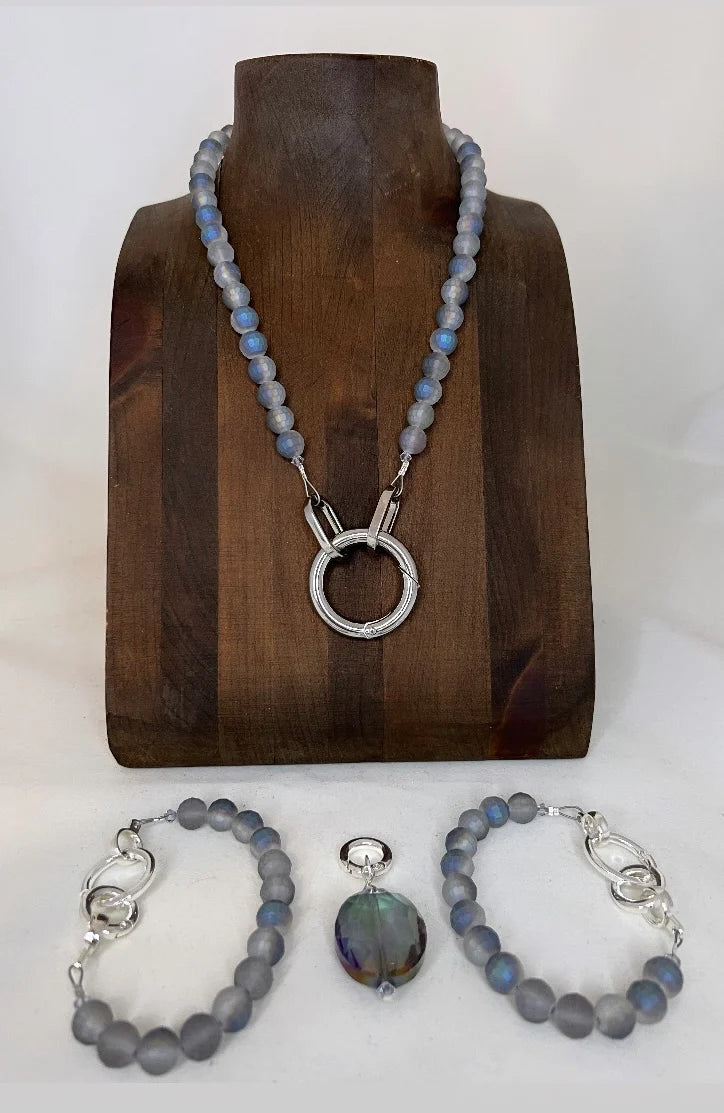 Jewelry set with necklace, bracelet, and pendant on a wooden stand.