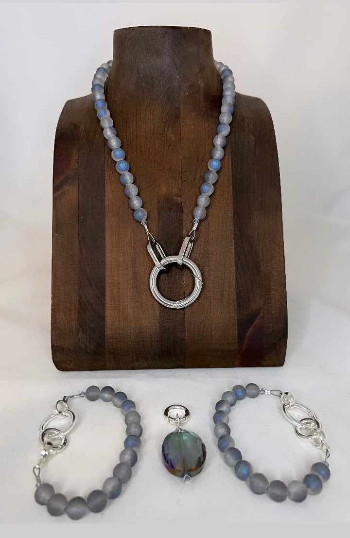 Jewelry set with necklace, bracelet, and pendant on a wooden stand.
