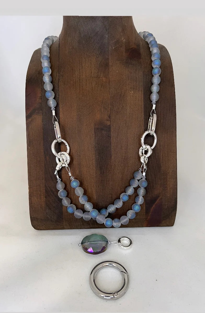 Necklace with blue beads and silver clasp on a wooden stand, with a pendant and ring displayed below.