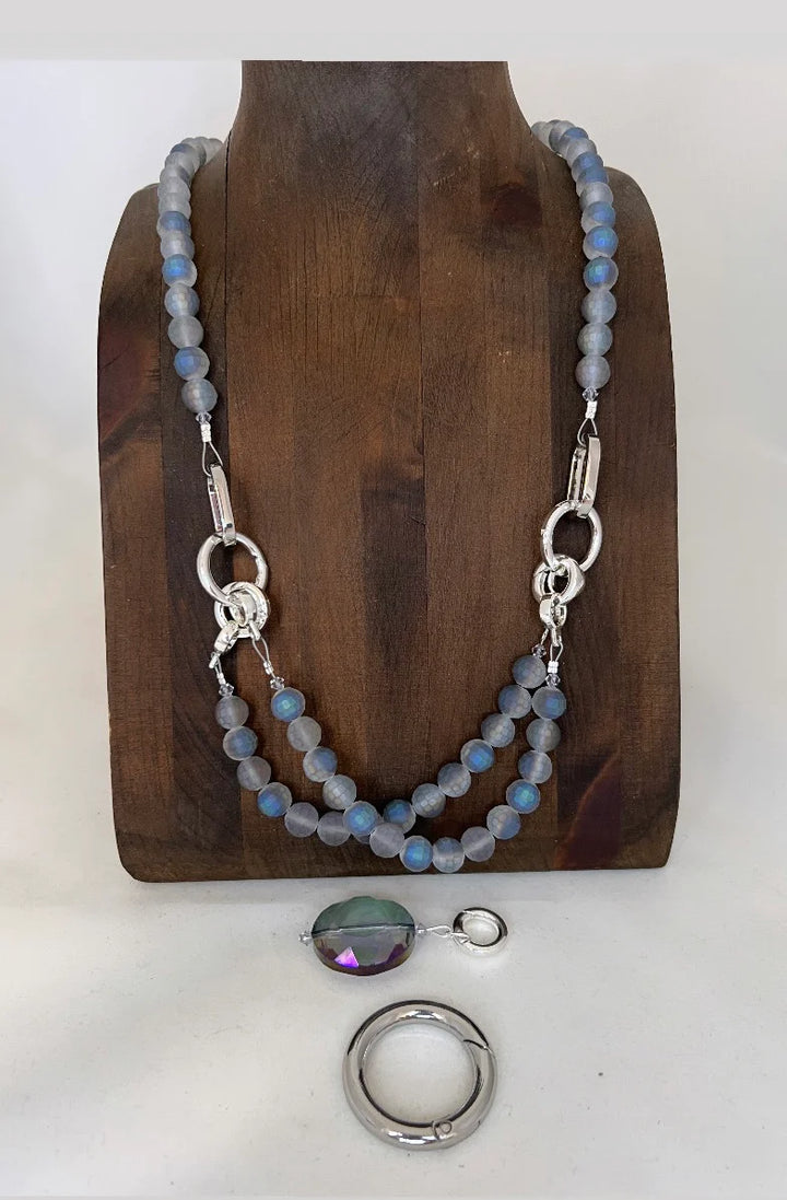 Necklace with blue beads and silver clasp on a wooden stand, with a pendant and ring displayed below.