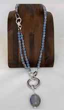 Necklace with blue beads and a heart-shaped pendant on a wooden stand.