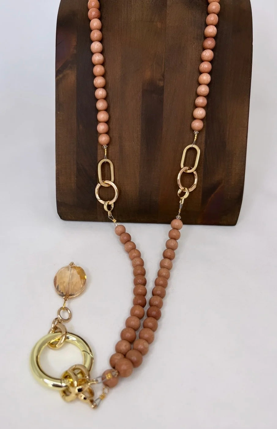 Necklace with wood and brown beads and gold accents on a wooden stand.