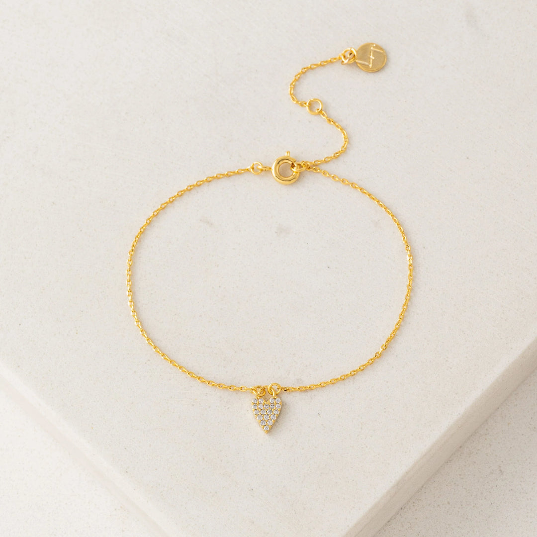 Gold bracelet with a heart-shaped charm on a light beige background