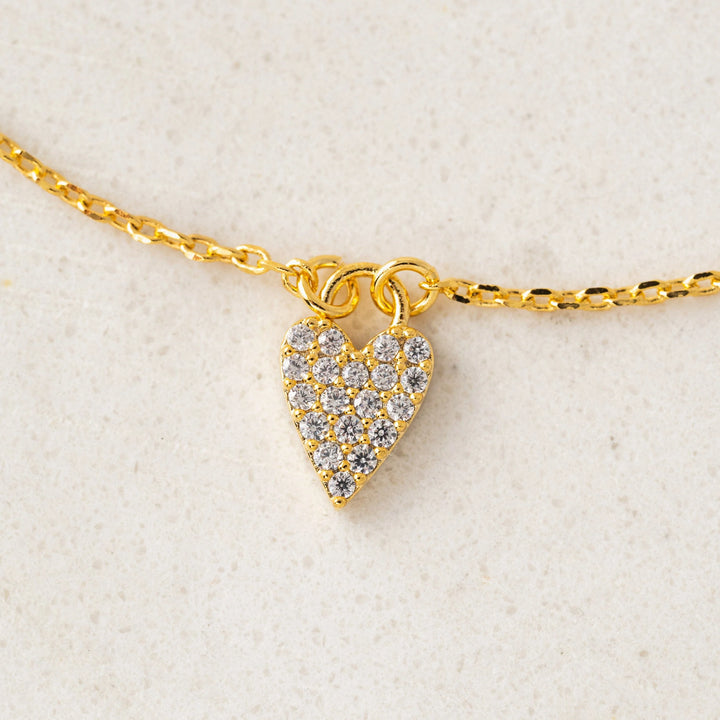 Gold necklace with a heart-shaped pendant on a light beige background