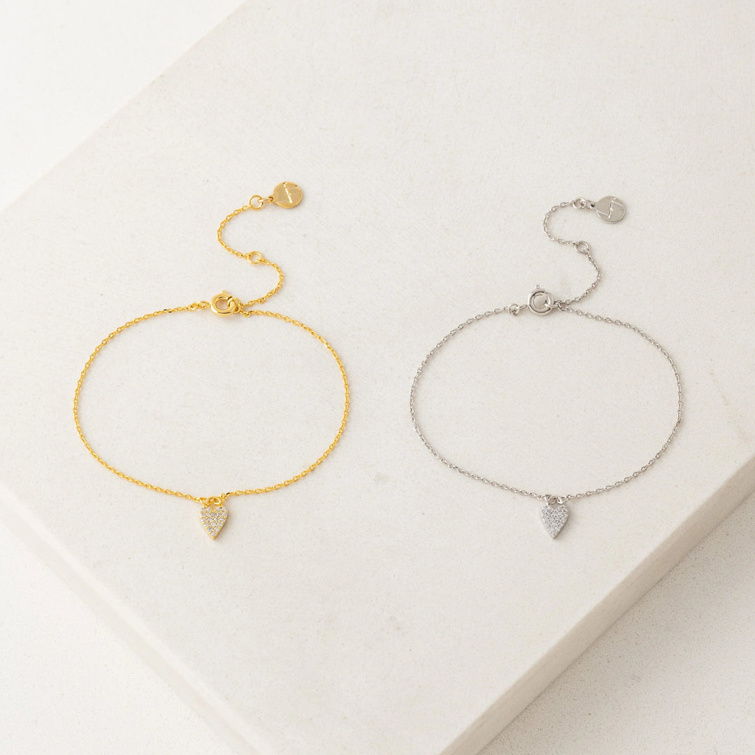 Gold and silver bracelets with heart-shaped charms on a light background