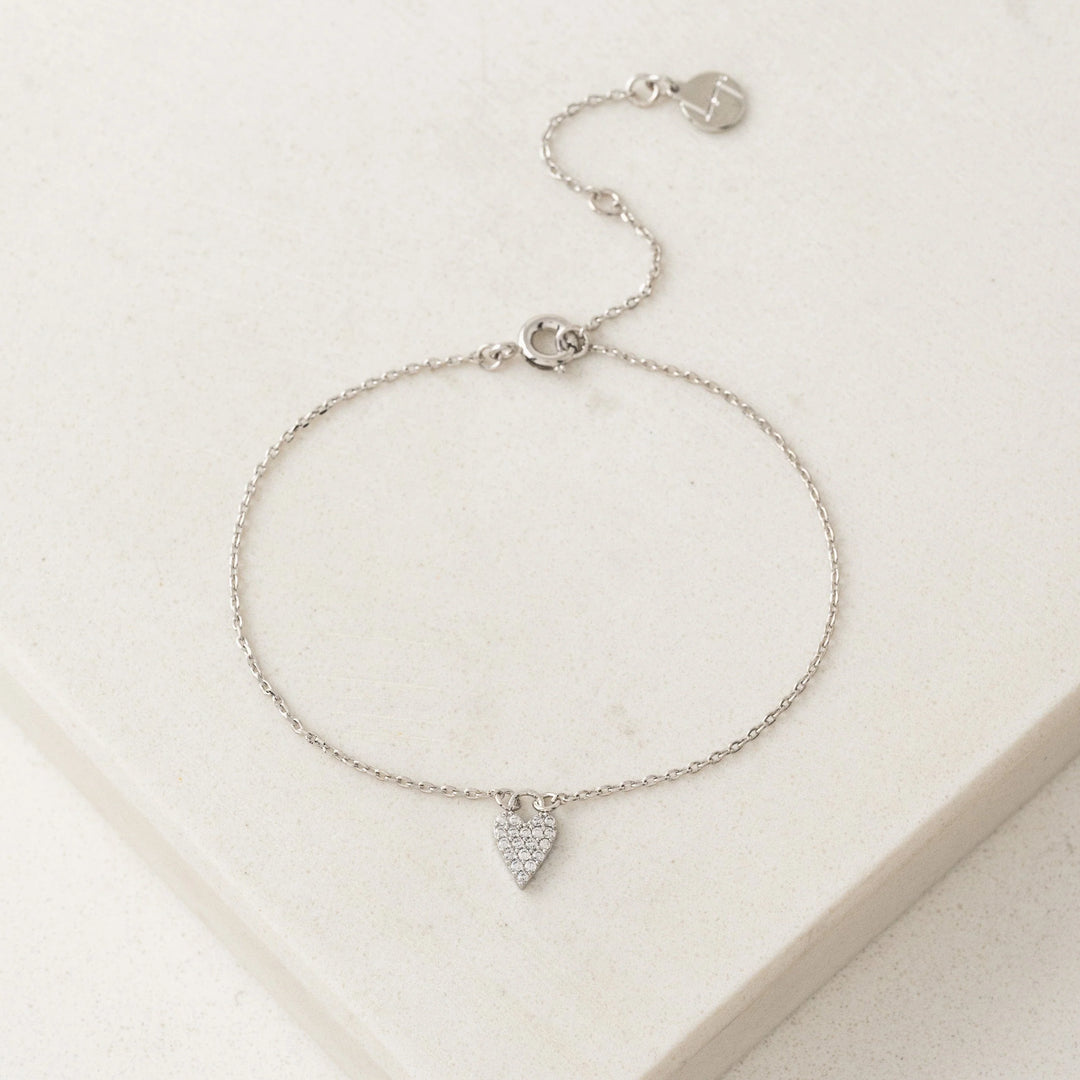 Silver bracelet with a heart-shaped charm on a light beige background