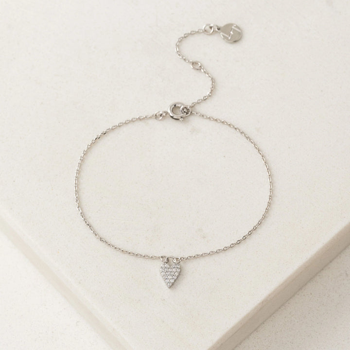 Silver bracelet with a heart-shaped charm on a light beige background