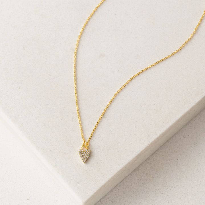 Gold necklace with a heart-shaped pendant on a light gray surface