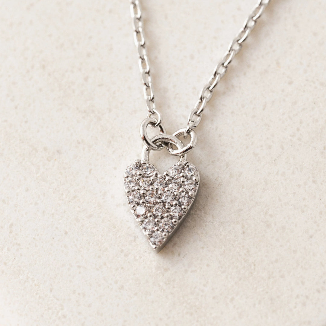 Silver heart-shaped pendant necklace on a light beige background
