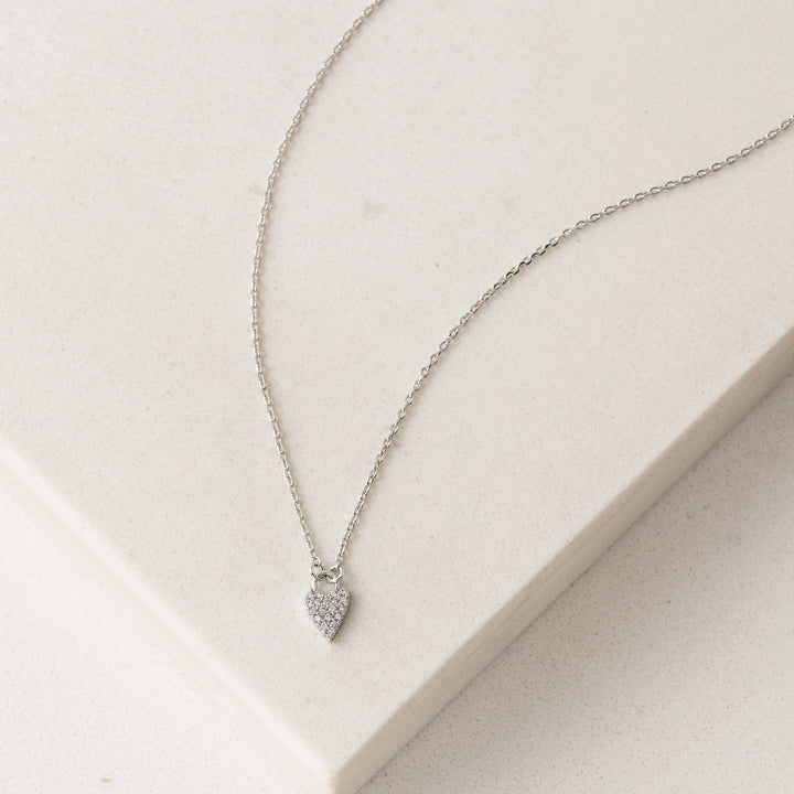 Silver necklace with a heart-shaped pendant on a light beige surface
