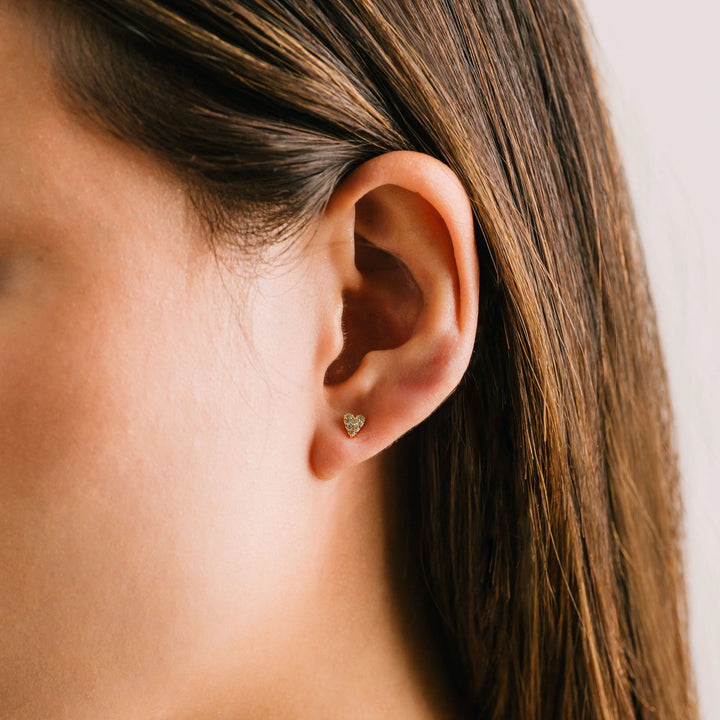 Close-up of an ear with a heart-shaped earring against a neutral background
