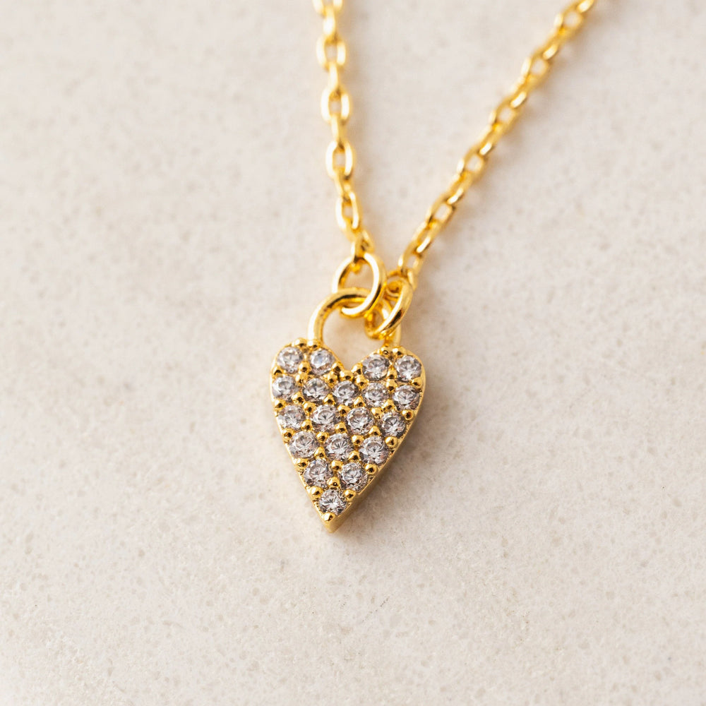 Gold heart-shaped necklace with embedded stones on a light beige background