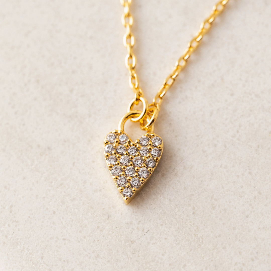 Gold heart-shaped necklace with embedded stones on a light beige background
