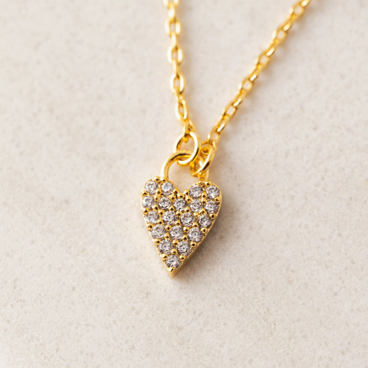 Gold heart-shaped necklace with embedded stones on a light beige background