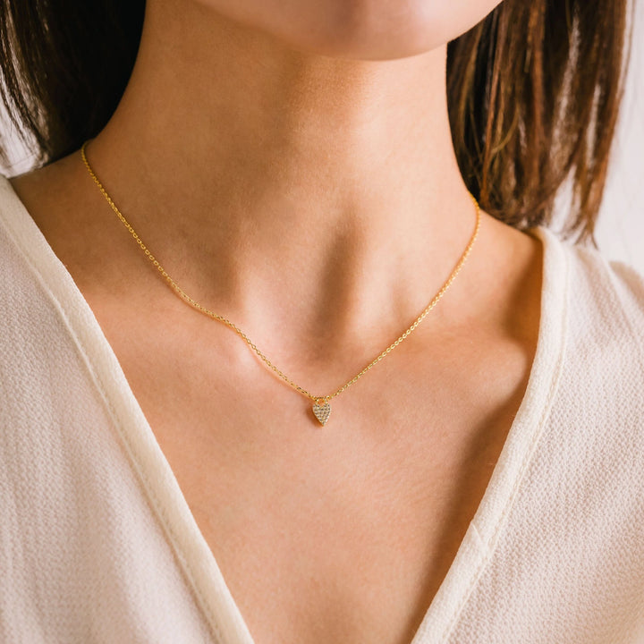 Gold necklace with a heart pendant on a person wearing a white top.