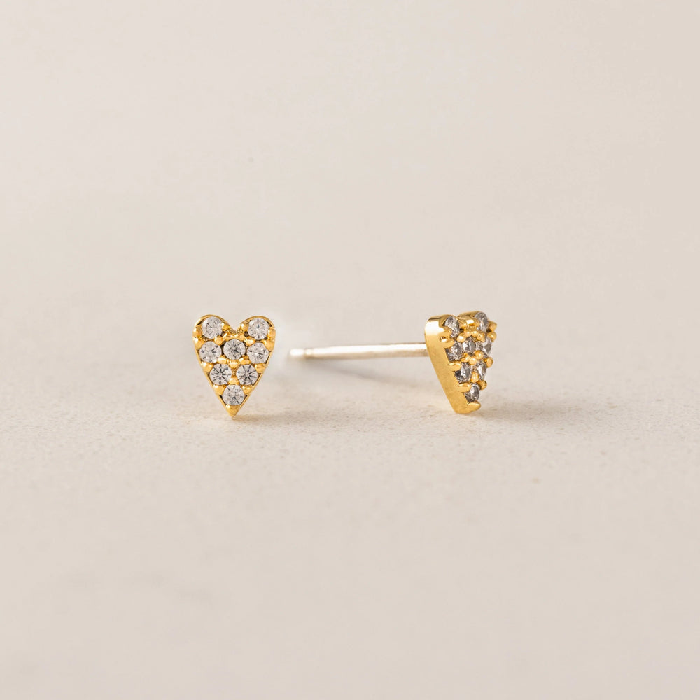 Heart-shaped gold earrings with embedded stones on a beige background