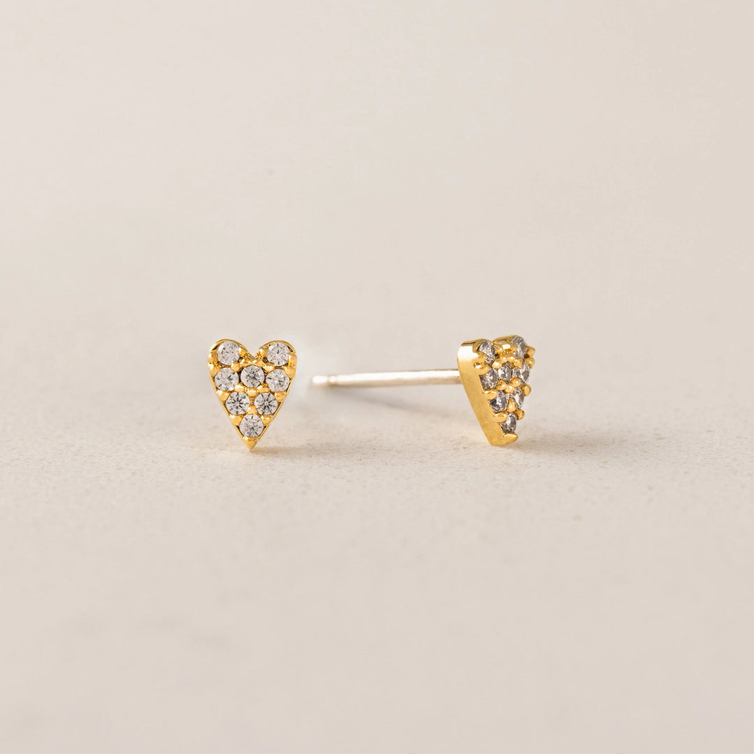 Heart-shaped gold earrings with embedded stones on a beige background