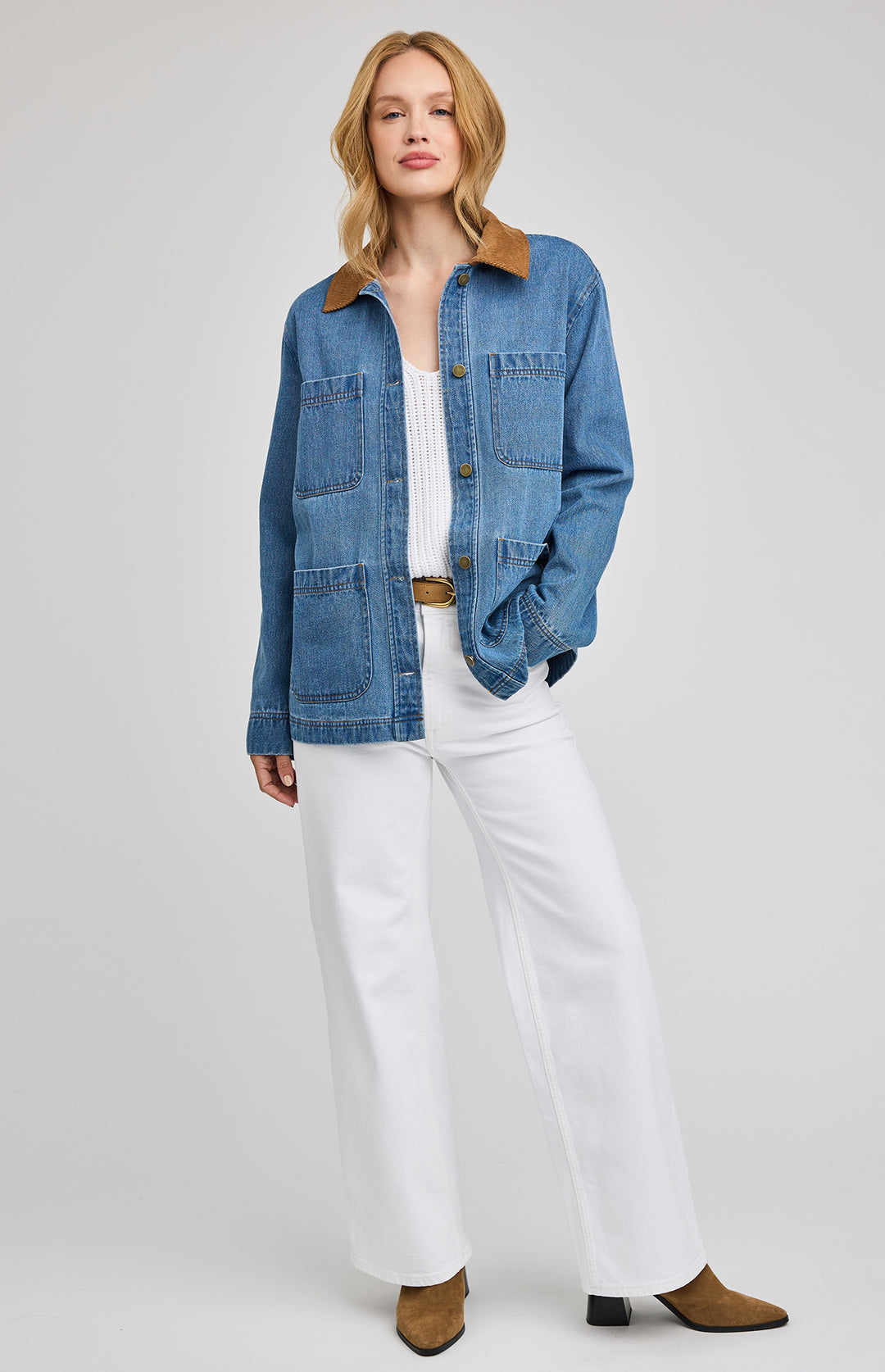 Woman wearing a blue denim barn jacket over a white top and pants on a plain background