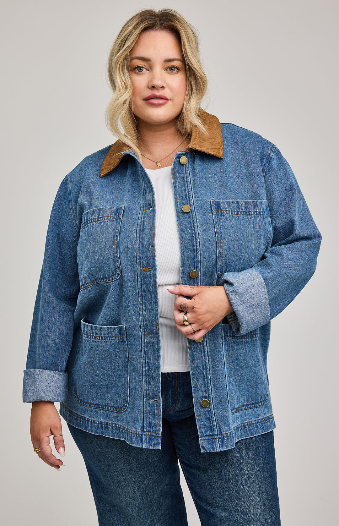 Woman wearing a blue denim barn jacket with a brown collar on a plain background