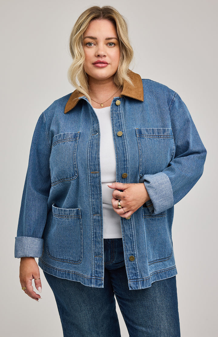Woman wearing a blue denim barn jacket with a brown collar on a plain background